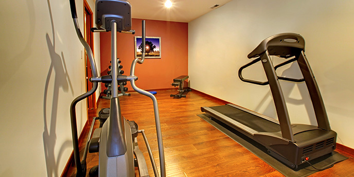 Elliptical and Treadmill Machines on Hardwood Floor in Basement Home Gym.