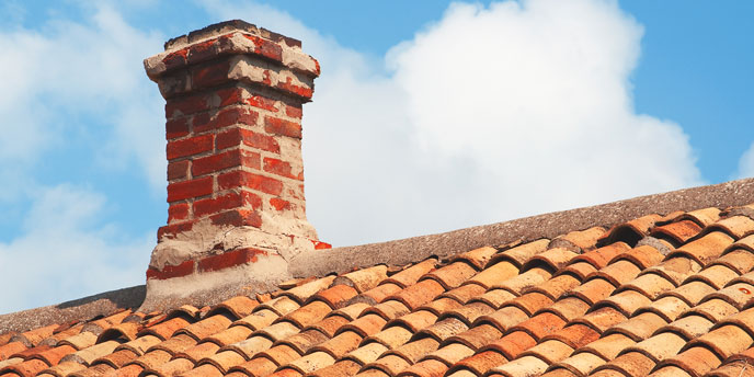 Brick Chimney on Terracotta Roof in Front of Partly Cloudy Skies